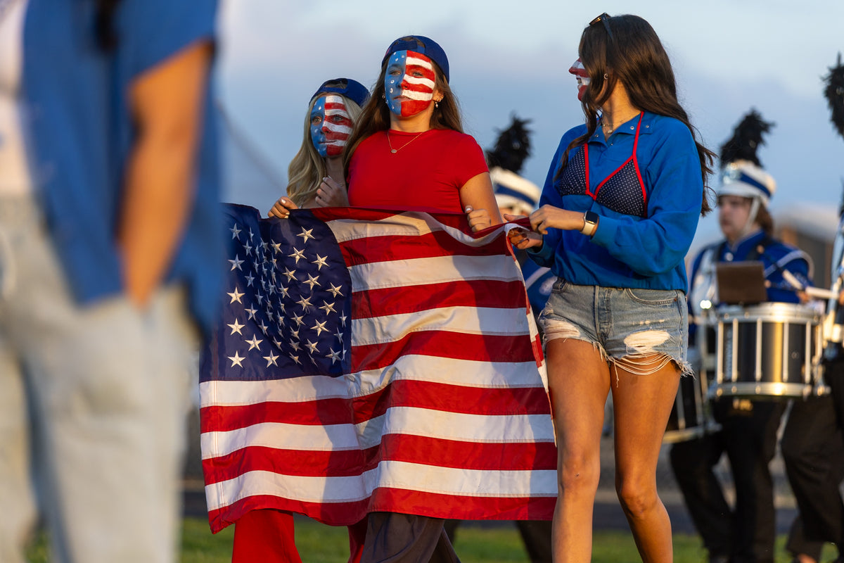 Clifton Central students with red, white, and blue face paint holding an American flag in the student section on Cheer Camp Night, Comets vs. BHRA football, August 28, 2026